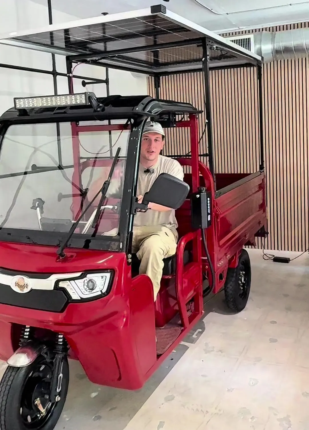 Francisco sentado en un triciclo eléctrico rojo con techo solar, dentro de la tienda